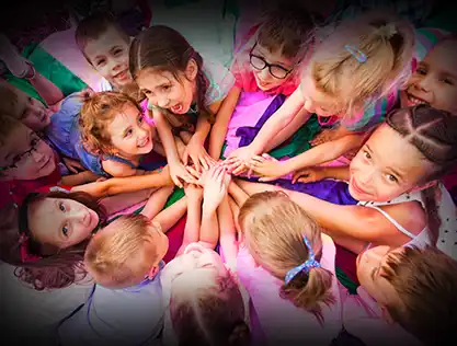 Group of happy children smiling and stacking hands in a circle during a fun outdoor activity